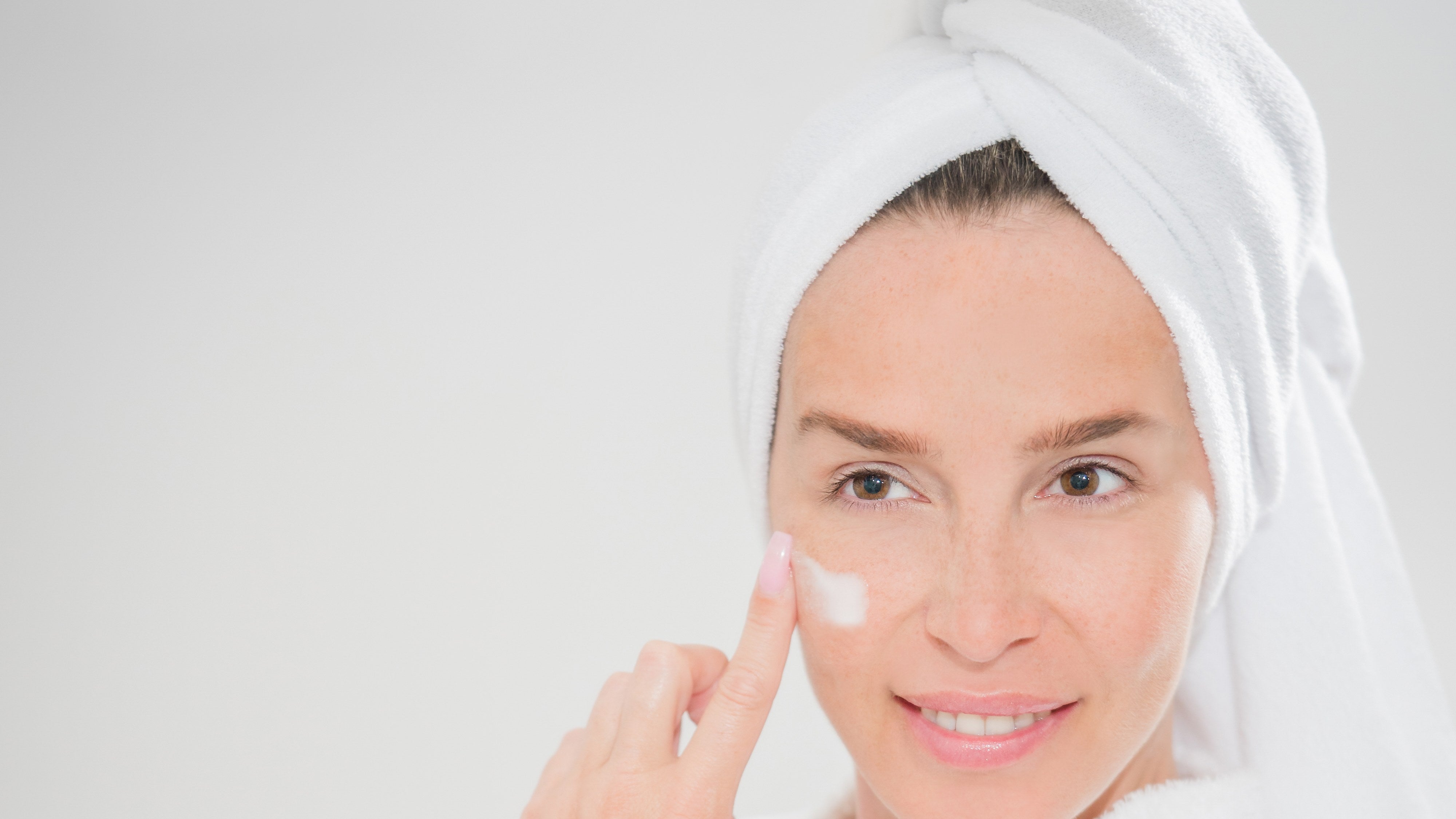 Femme en peignoir appliquant sa crème de soin du visage